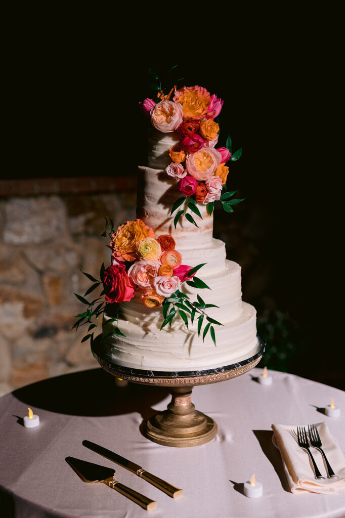 5-tier semi-naked wedding cake with colorful orange, pink and yellow flowers.