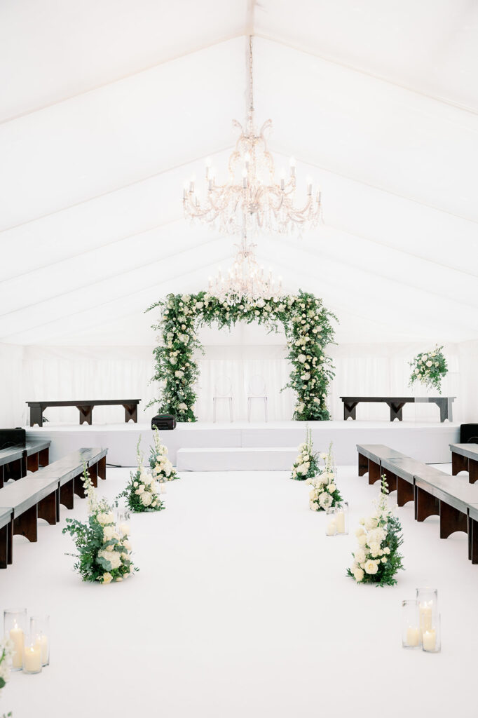 Contemporary runway-style wedding ceremony with white and greenery floral arrangements.
