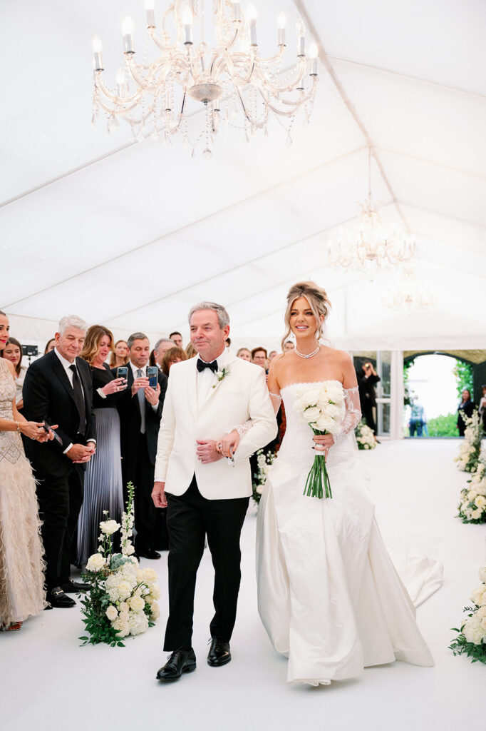 Bride linking arms with her dad walking down the of her tent ceremony.