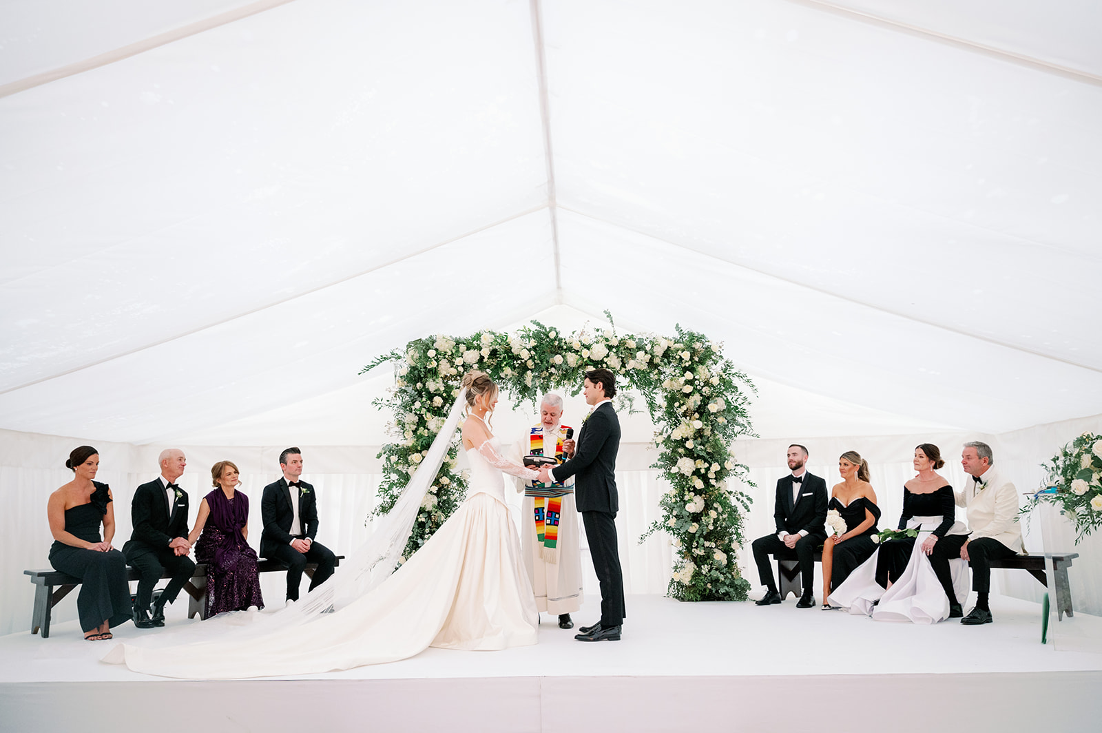 Beautiful contemporary wedding ceremony in a tent with a large floral arch.