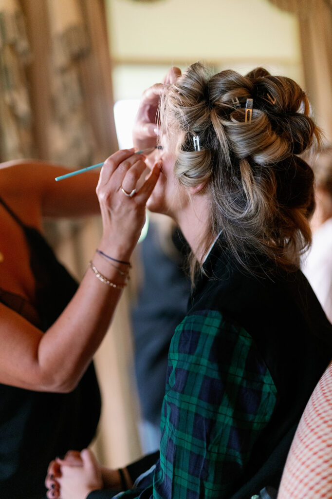 A bride with her hair pinned getting her makeup done for her wedding.