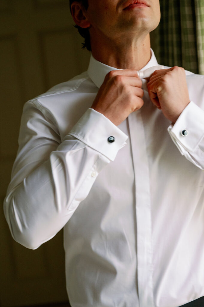 Groom getting ready putting on his white bowtie.