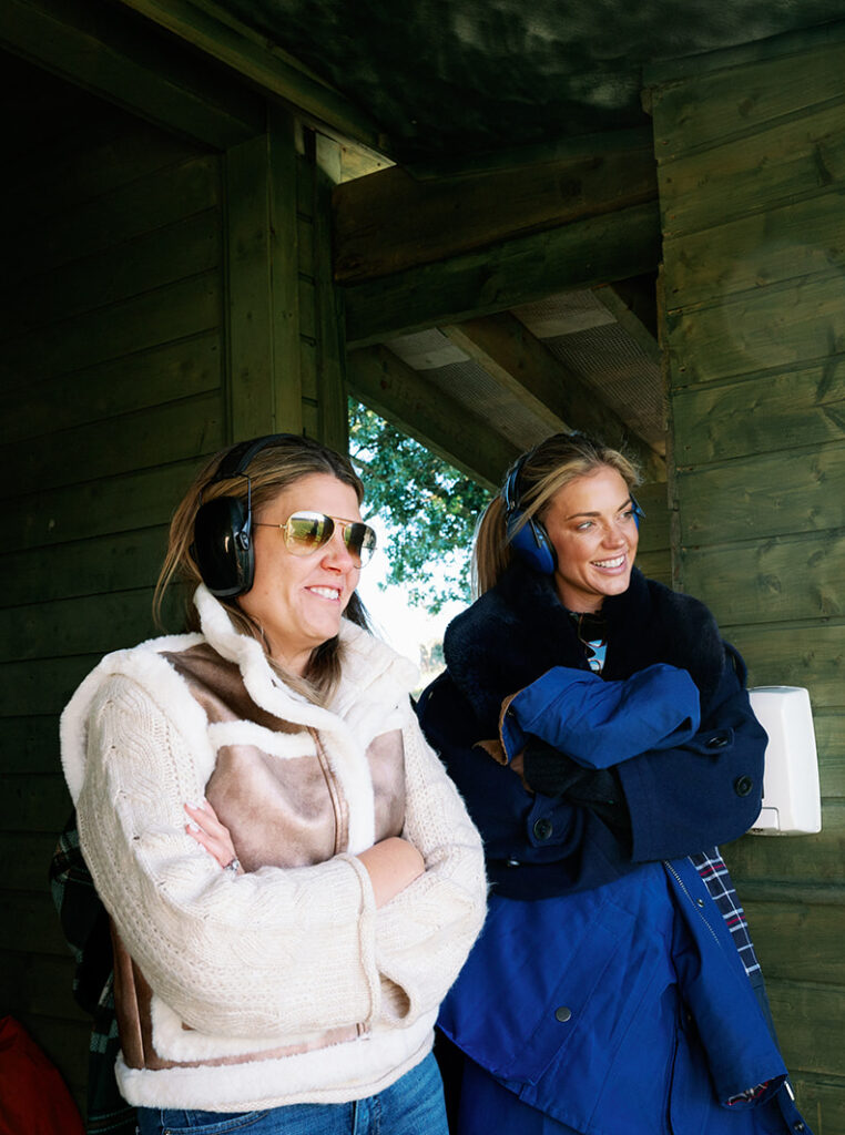 A bride and her mom wearing ear muffs while watching her husband shoot a gun at Ballyfin Demesne.