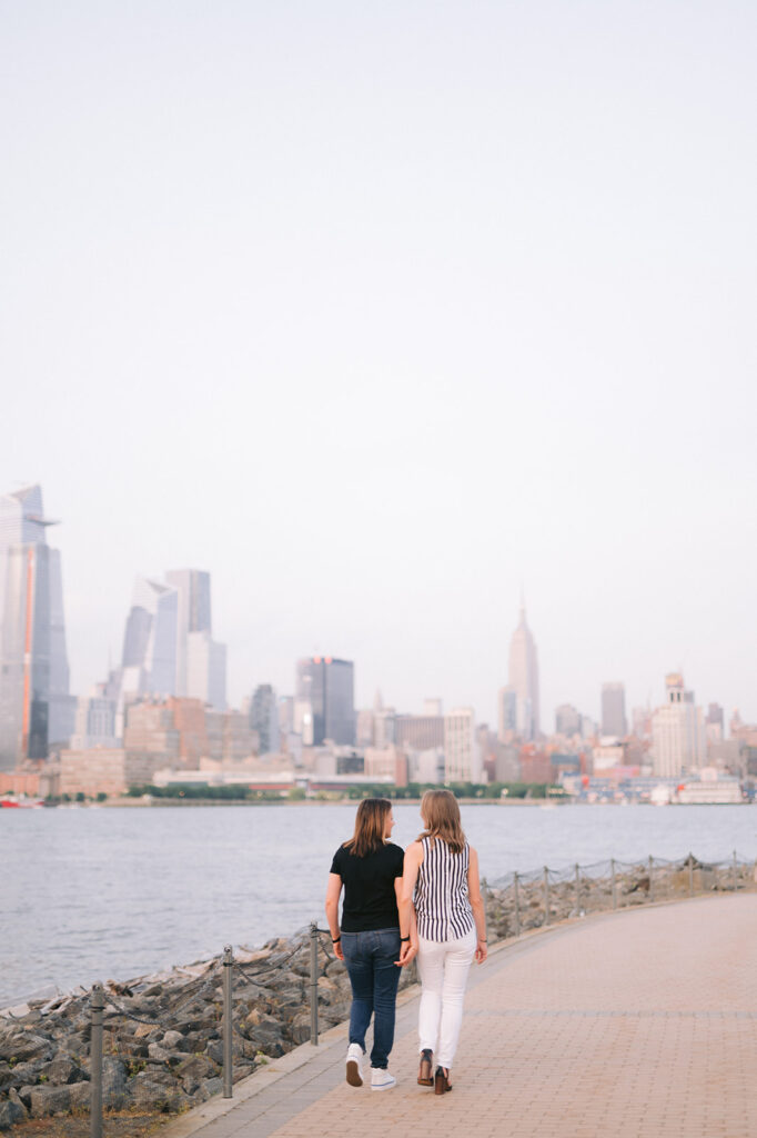 Couple walking on a path in Jersey City with a view of the Manhattan skyline. 