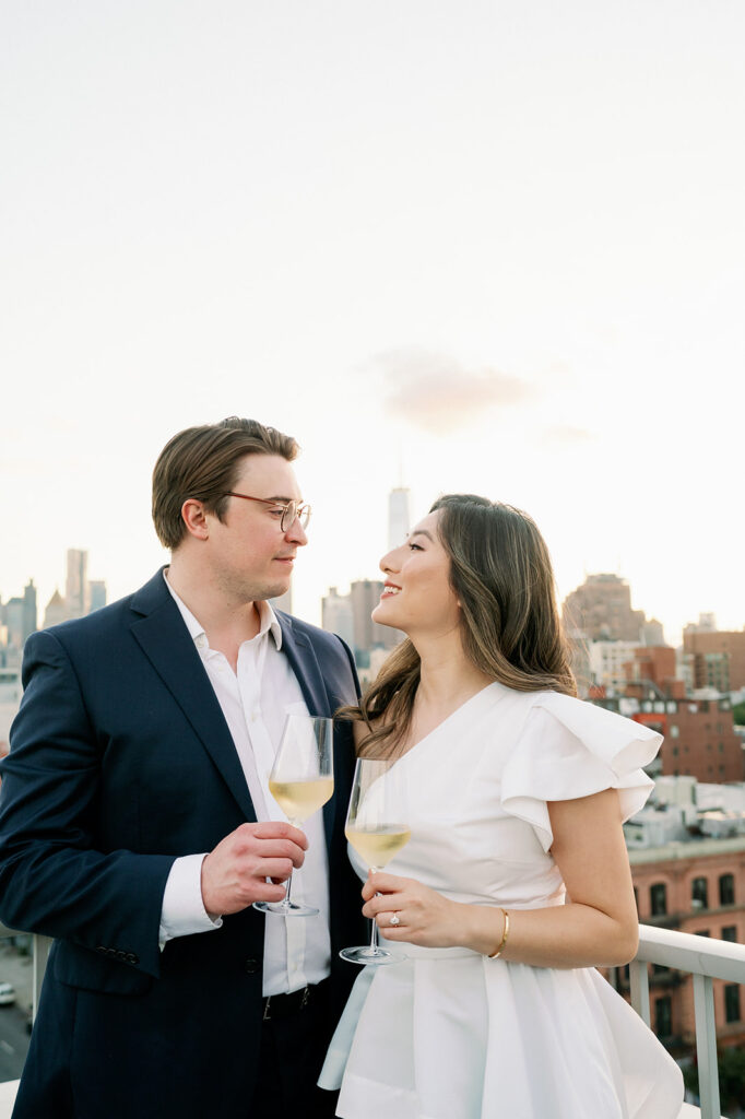 Couple drinking wine on a rooftop overlooking Manhattan for their engagement photo session. 