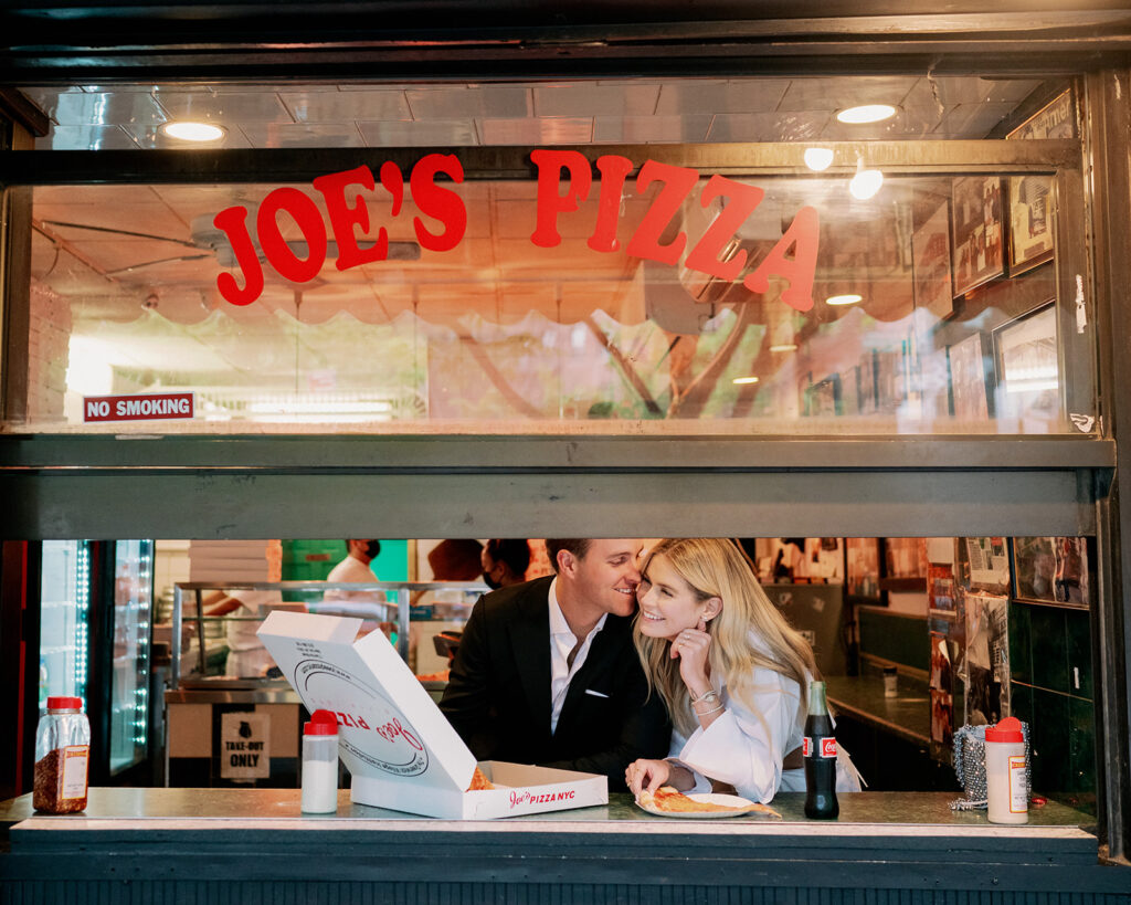 Couple sitting under the window of Joe's Pizza in NYC for their engagement photo session.