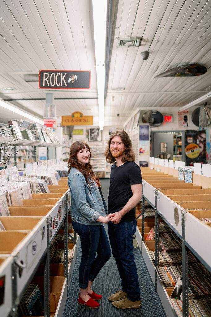 Couple posing in an aisle of a NYC record shop for their engagement photos.