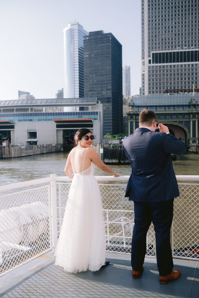 Elegant couple wearing sunglasses holding onto the railing of a New York City ferry boat. 