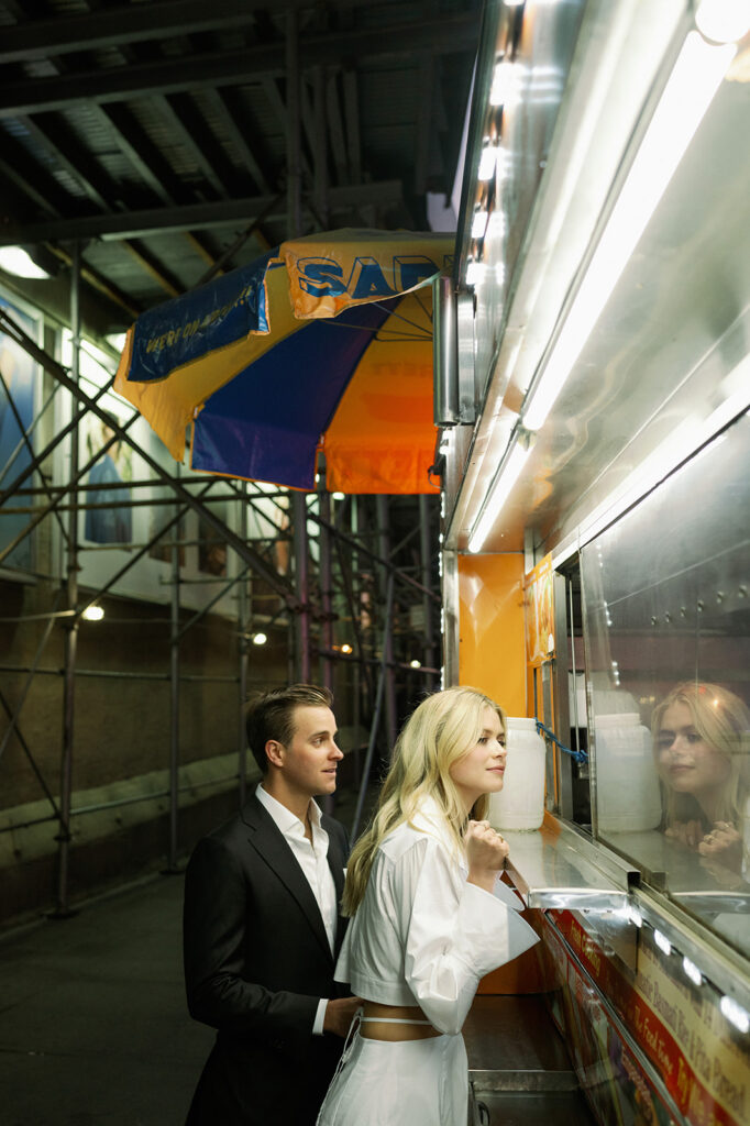 Couple ordering a late night hot dog in New York after their engagement photos. 
