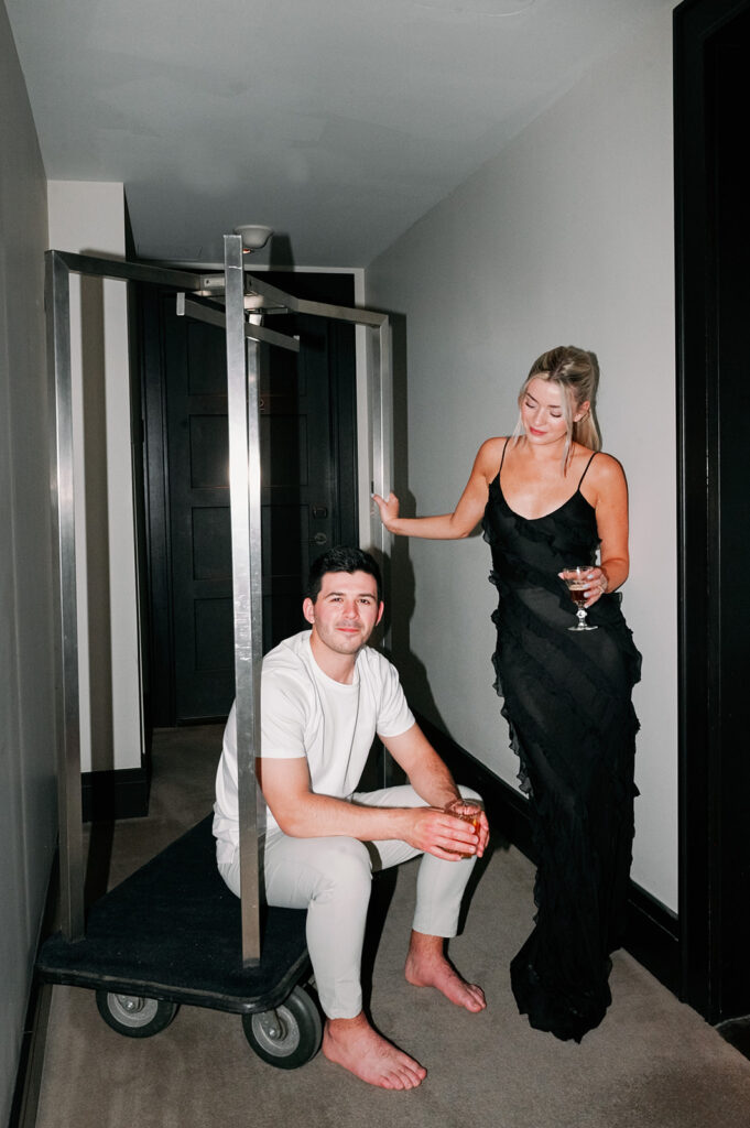 Couple posing on a luggage cart inside their NYC hotel suite. 