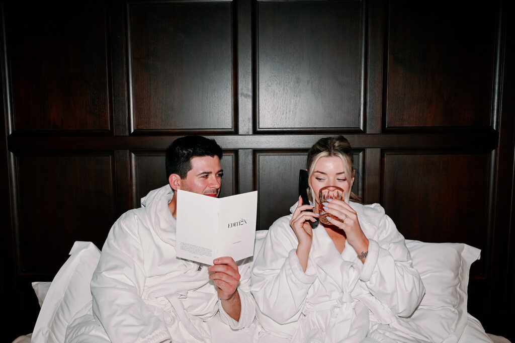 Couple sitting in a New York hotel suite bed wearing robes and ordering room service. 