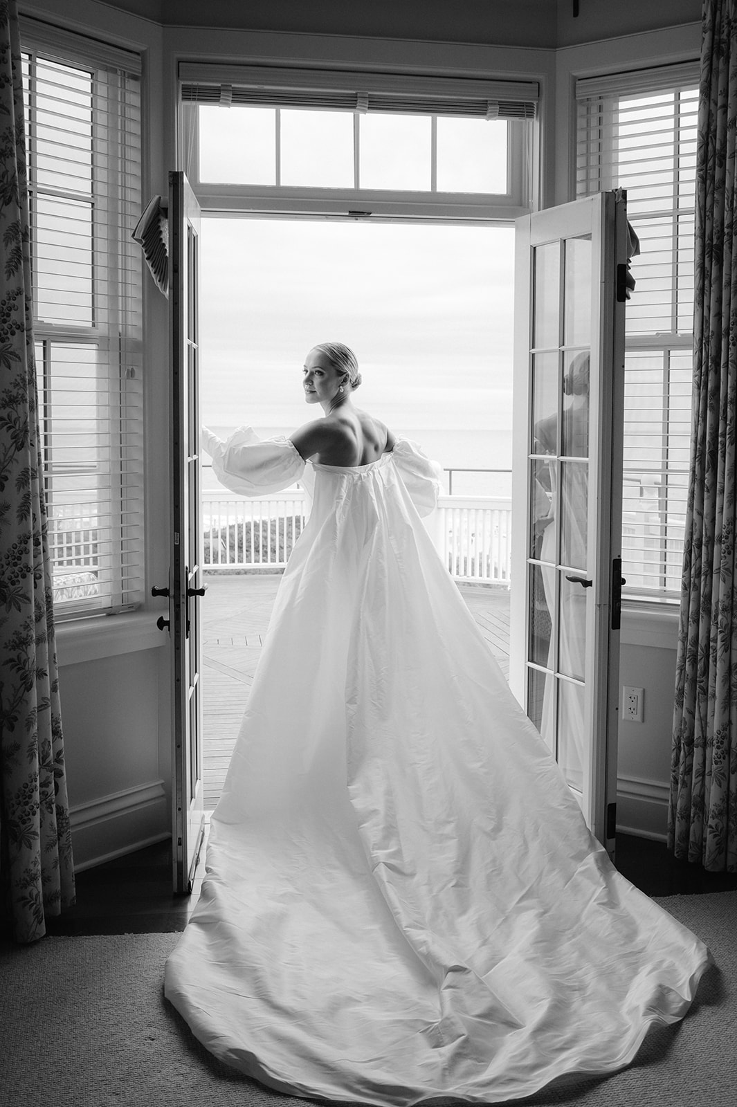 Romantic black and white editorial shot of a bride standing in the doorway of her hotel suite balcony on her wedding day. 