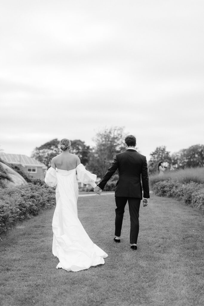 A black and white editorial capture of a bride and groom walking and holding hands after their first look. 
