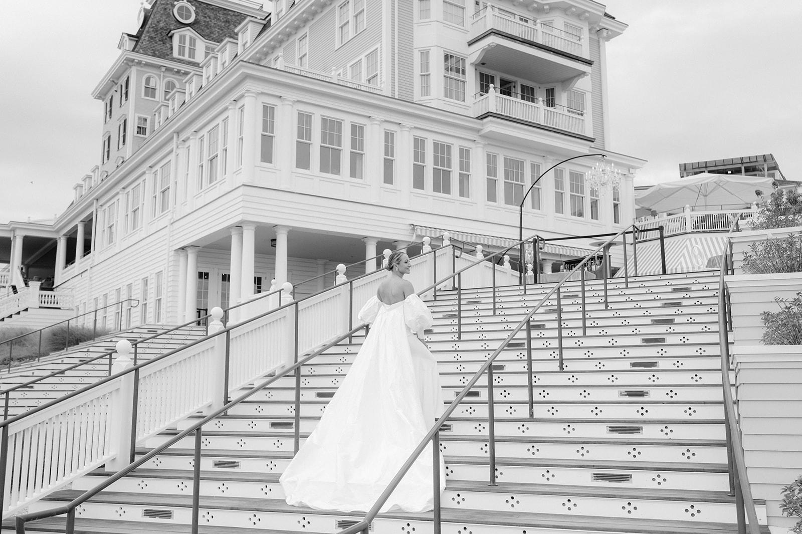 A black and white landscape shot of a bride walking up the stairs of Rhode Island's Ocean House. 