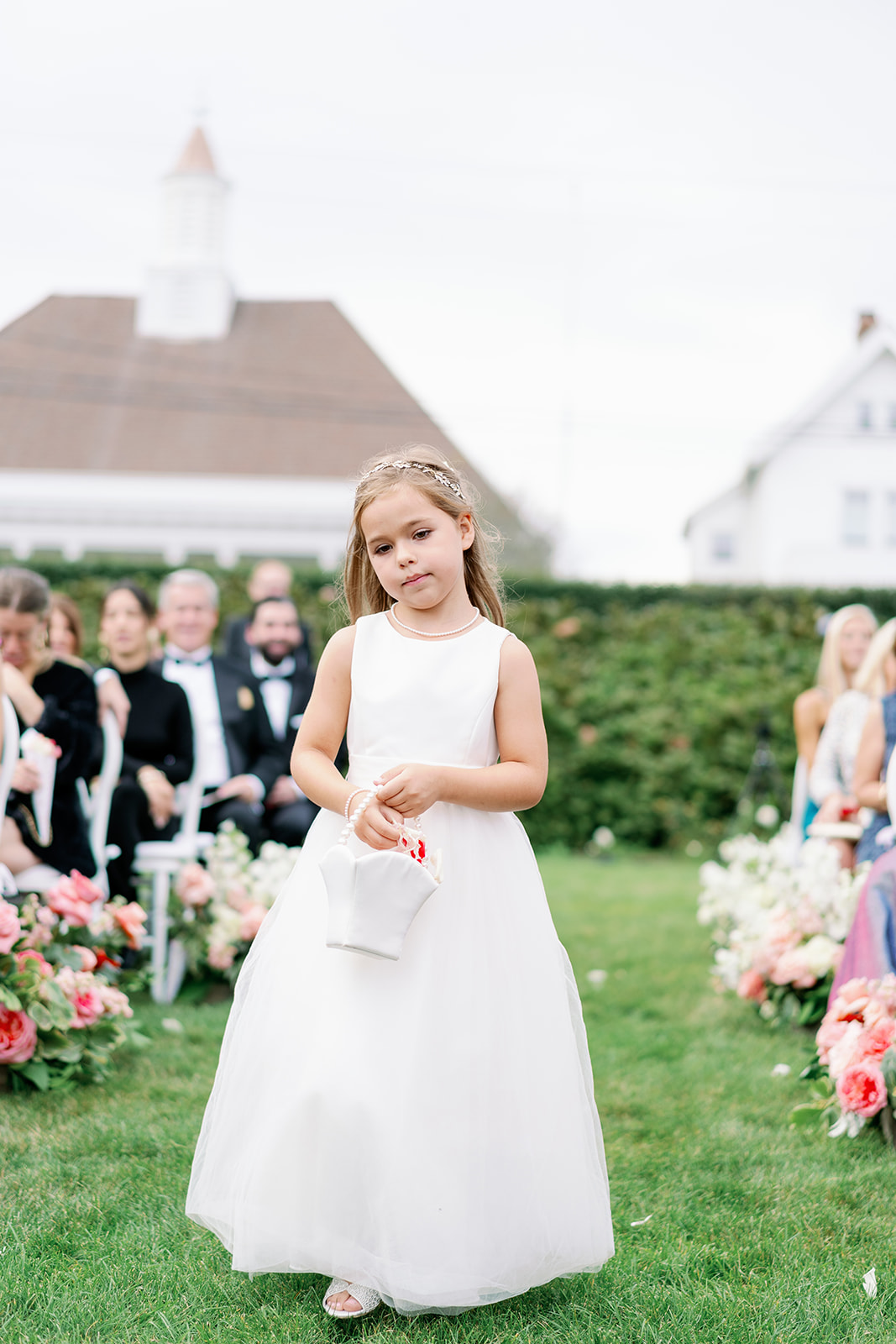 Cute flower girl in a white dress with a basket of petals walking down the aisle. 