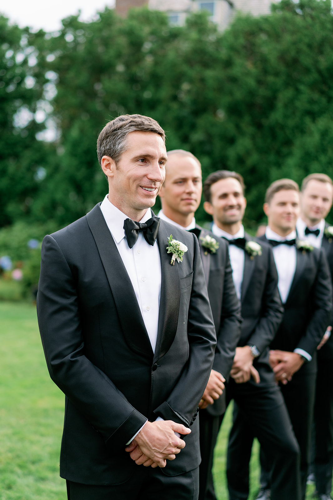 Groom smiling with his groomsmen in the background as he watches his bride walking down the aisle. 