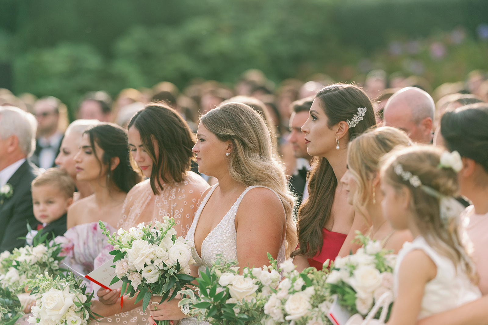 Candid shot of six bridesmaids sitting in the front row watching the wedding ceremony. 
