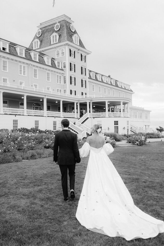 Editorial black and white capture of a bride and groom walking towards their venue Ocean House in Rhode Island.