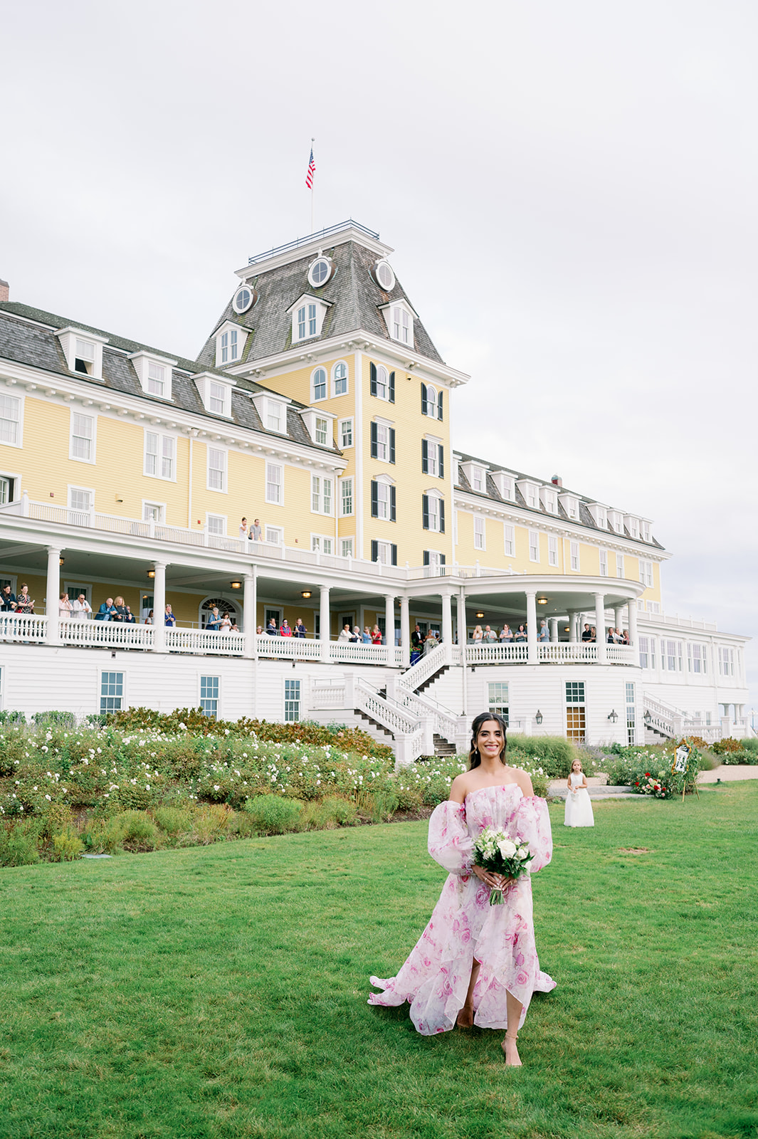 Maid of honor wearing a romantic floral dress walking down the aisle on the lawn of Ocean House in Rhode Island. 