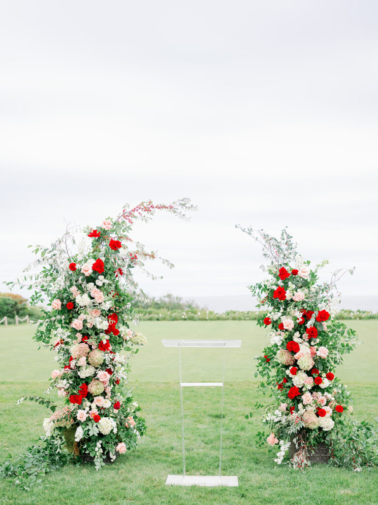 Romantic freestanding floral arch with red and pink roses, peonies and greenery on the lawn of Ocean House in Rhode Island.