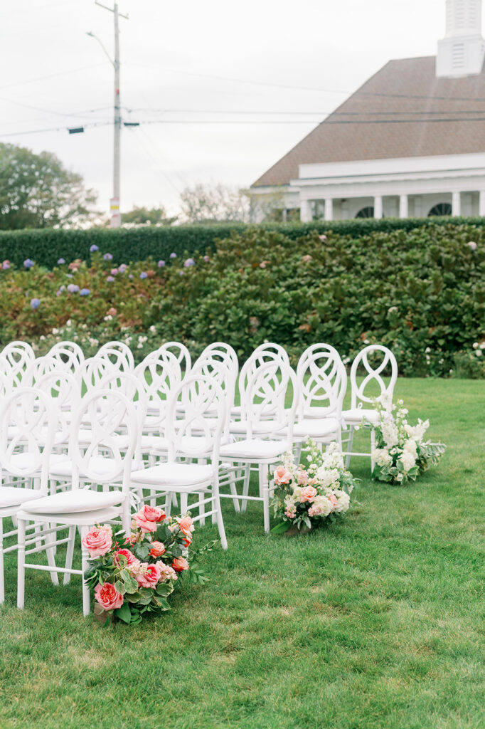 Wedding ceremony setup on the lawn of Ocean House in Rhode Island featuring a floral aisle and white chairs. 