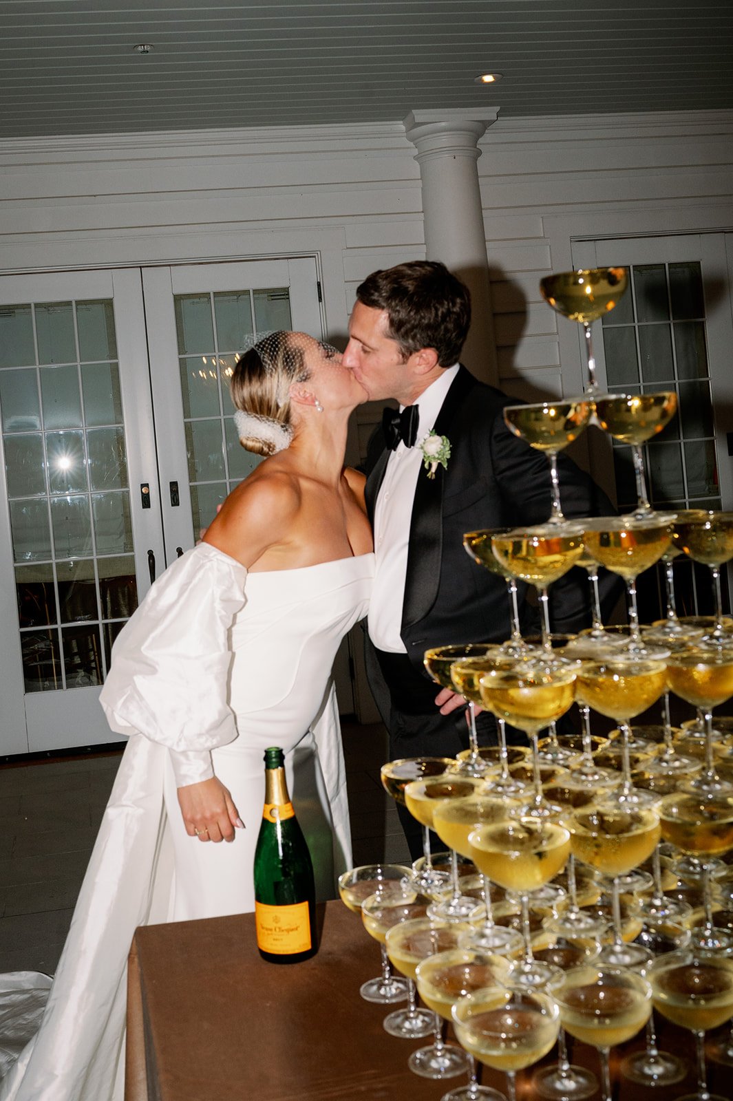 Bride and groom sharing a kiss behind a champagne tower. 