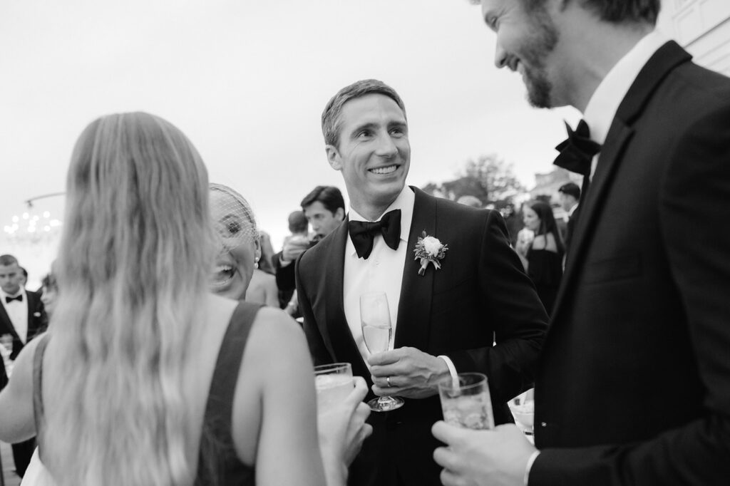 Candid shot of a bride and groom chatting with guests at cocktail hour of their Rhode Island wedding. 