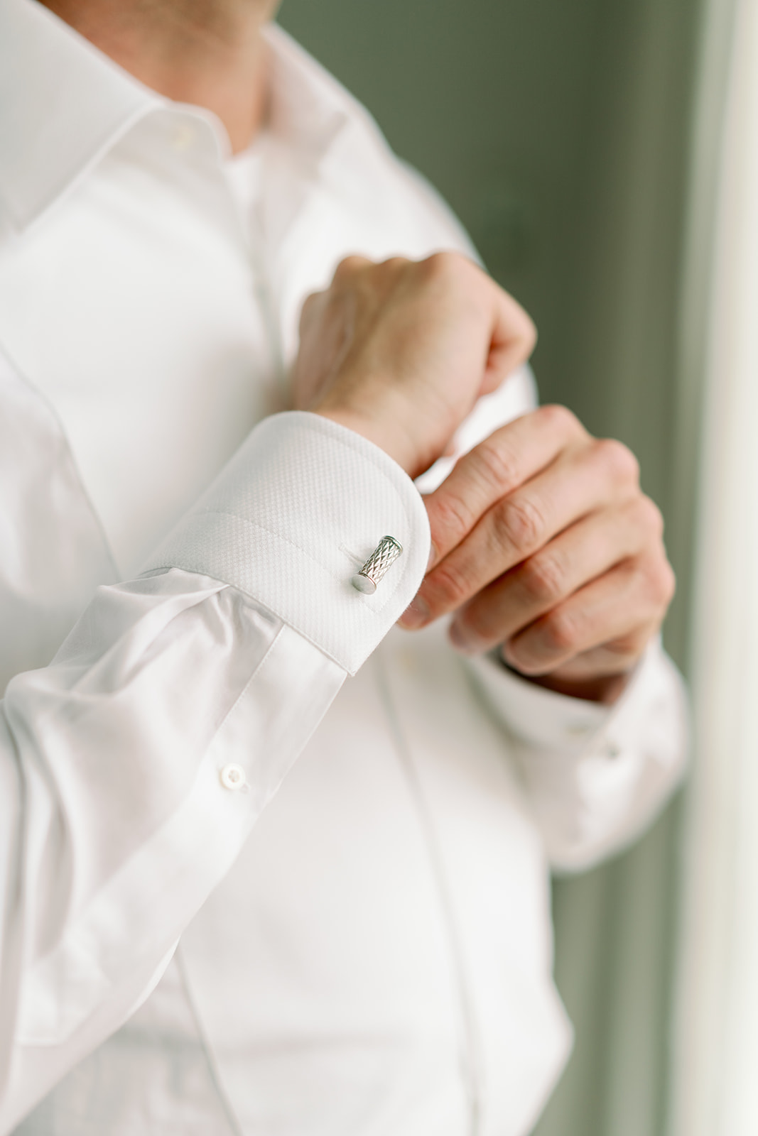 A close up shot of a groom putting on his cufflinks. 