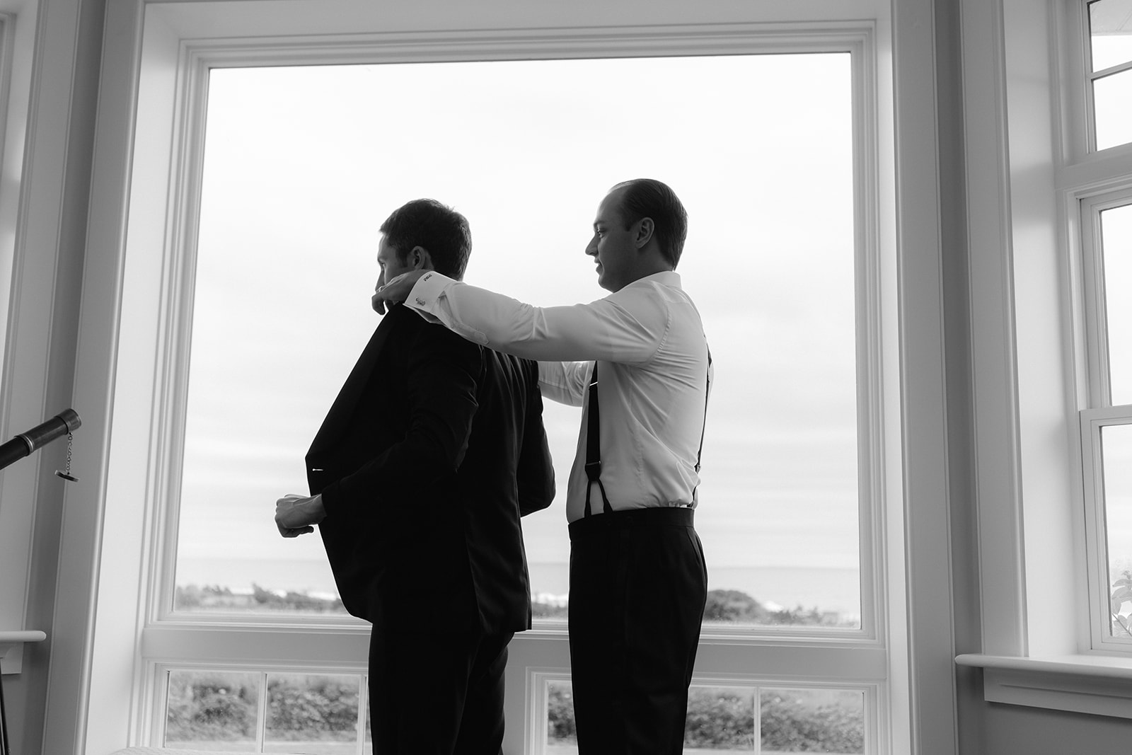 A groom getting his suit jacket put on by one of his groomsmen. 