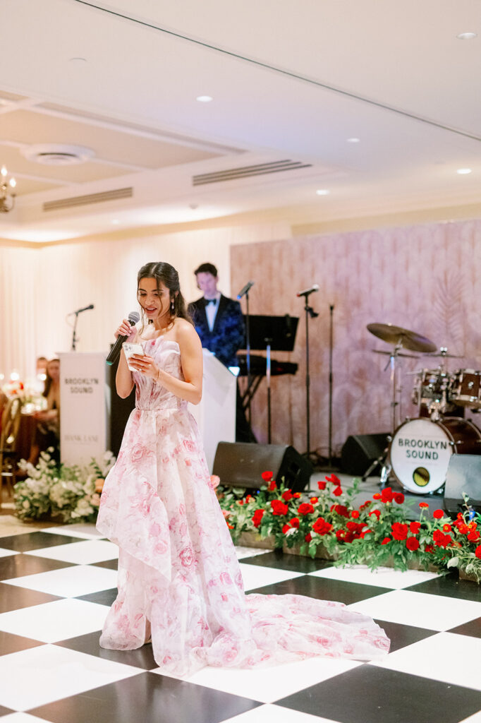 A maid of honor wearing a romantic floral dress giving a speech at the wedding reception. 