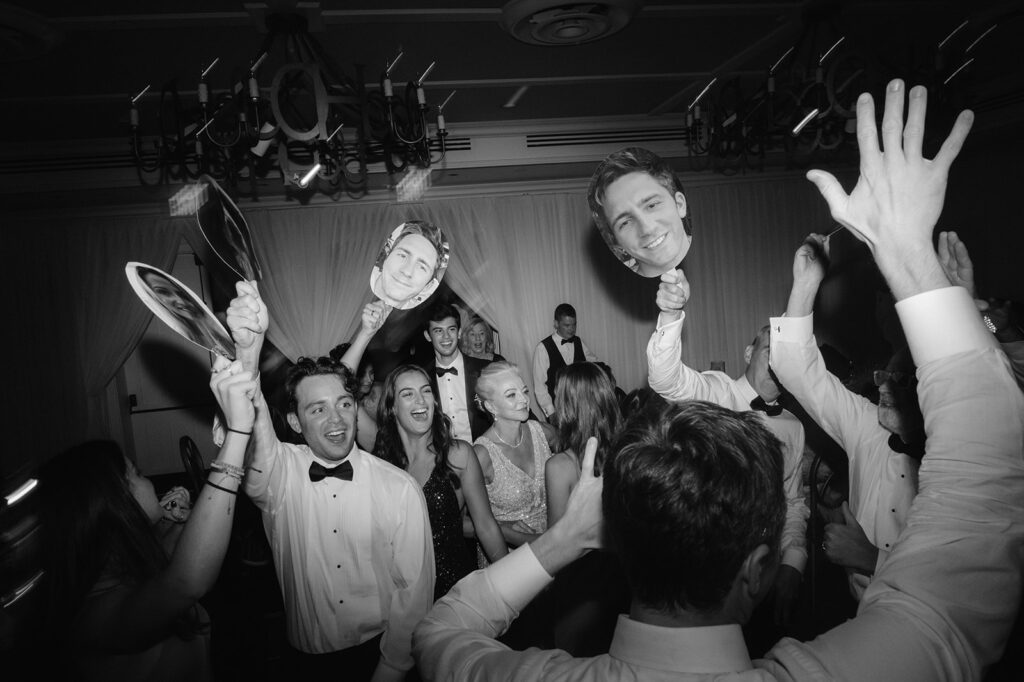 Wedding guests holding up signs of the groom's face during the reception dance party. 