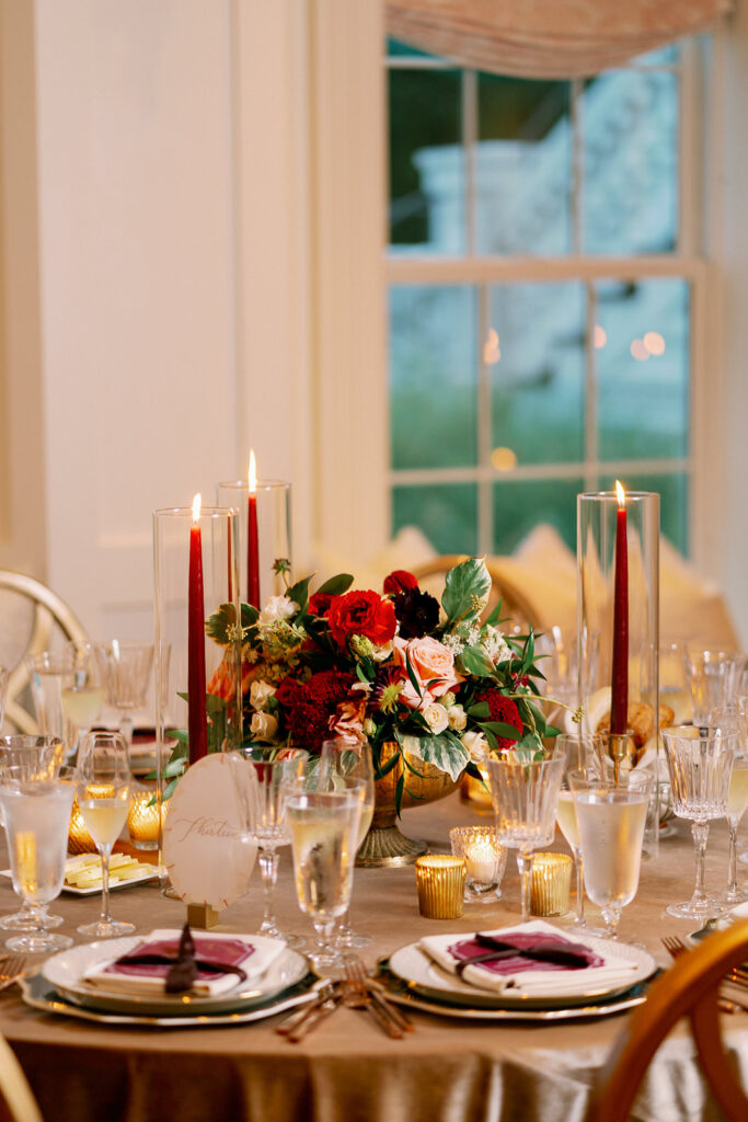 Romantic wedding reception table with candles, a gold tablecloth and red floral centerpiece. 