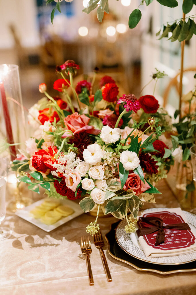 Extravagant wedding reception table red and blush floral centerpiece and place setting. 