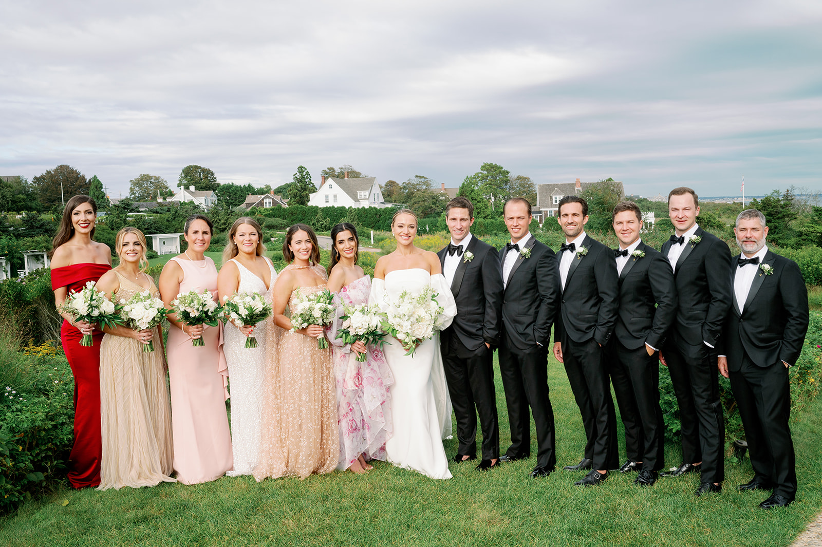 Romantic posed garden wedding party portrait with mismatched bridesmaid dresses and classic black groomsmen attire. 