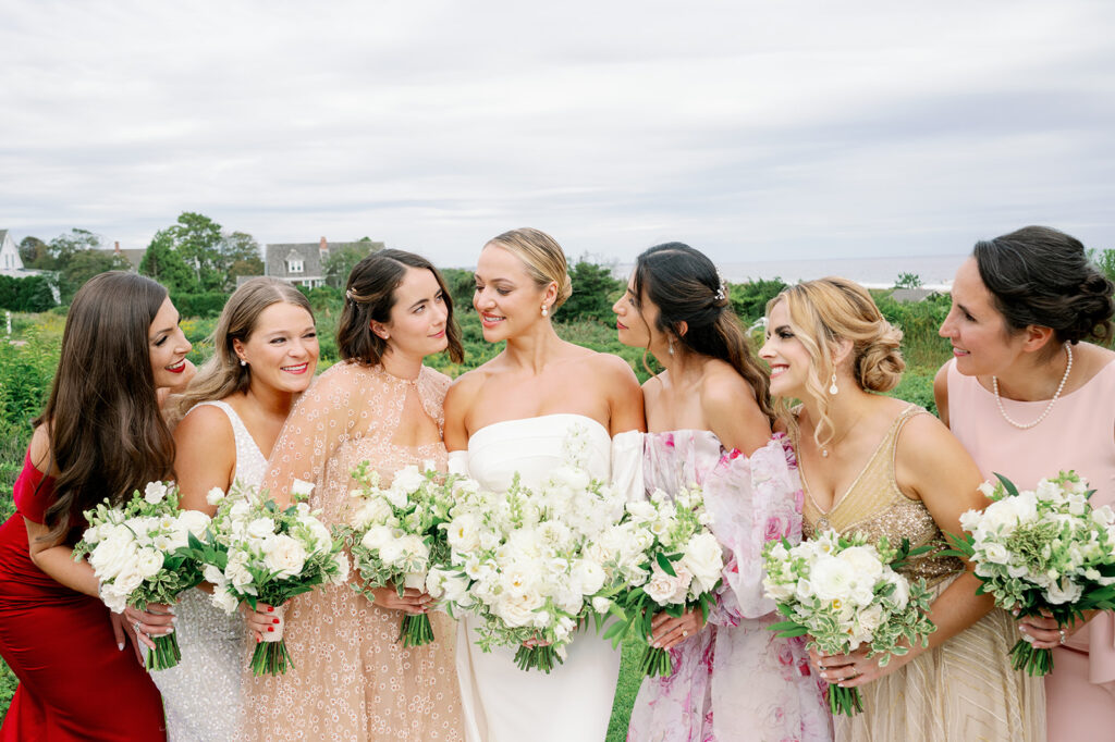 Elegant garden bridal party in mismatched dresses holding white rose floral bouquets.