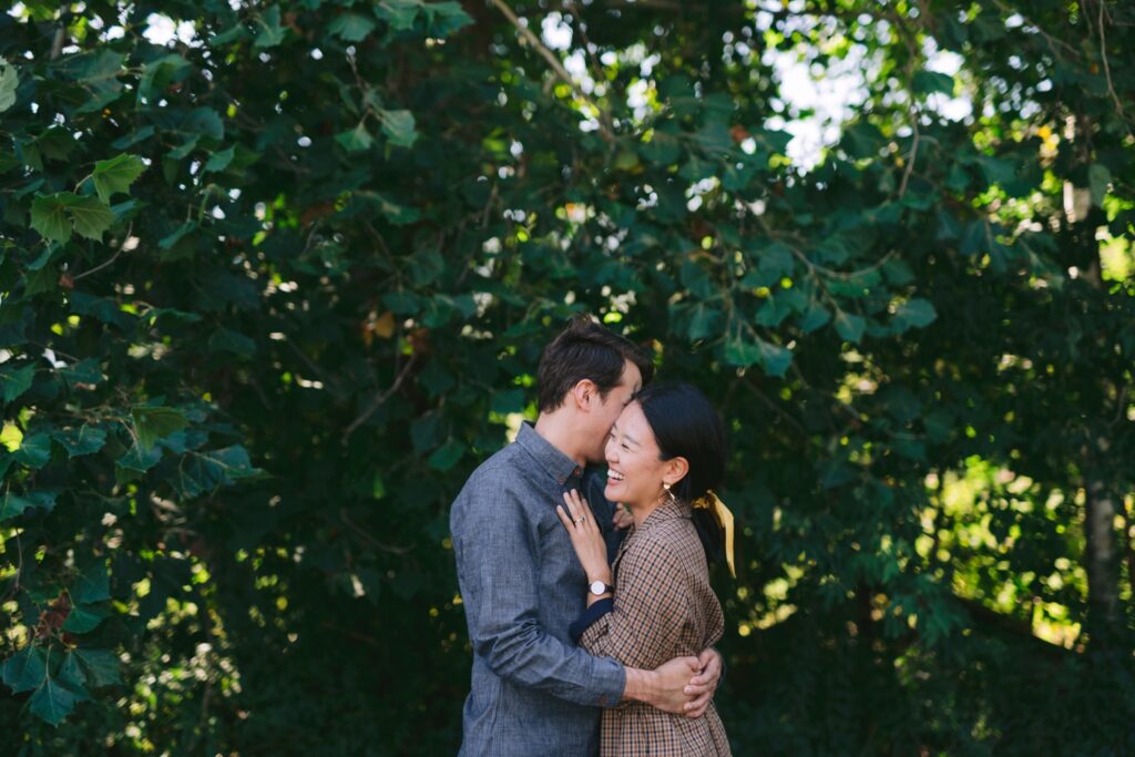 Couple embracing and smiling in front of a greenery backdrop in the Catskills in Hudson Valley. 