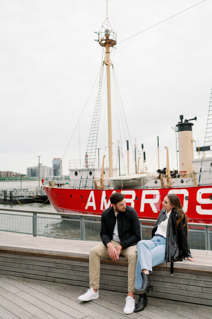 Couple sitting on a bench in South Street Seaport in NYC with a red sailboat in the background. 