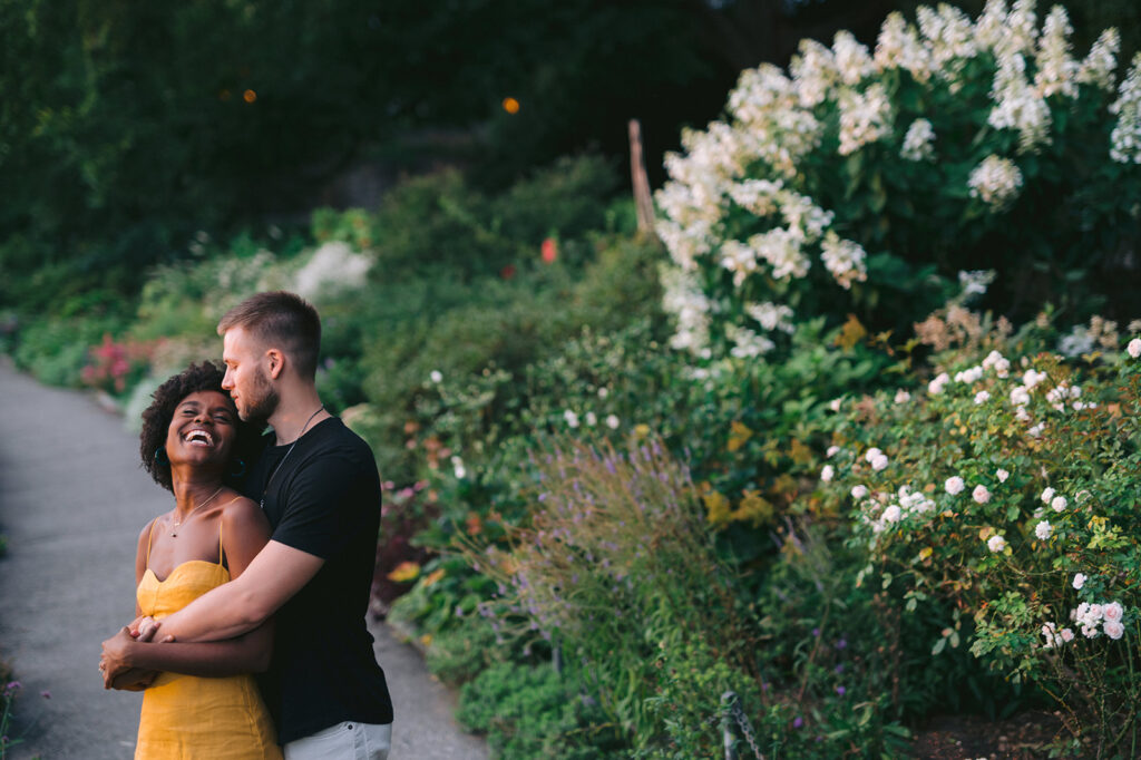 Couple embracing in front of a lush greenery background in Washington Heights in NYC. 