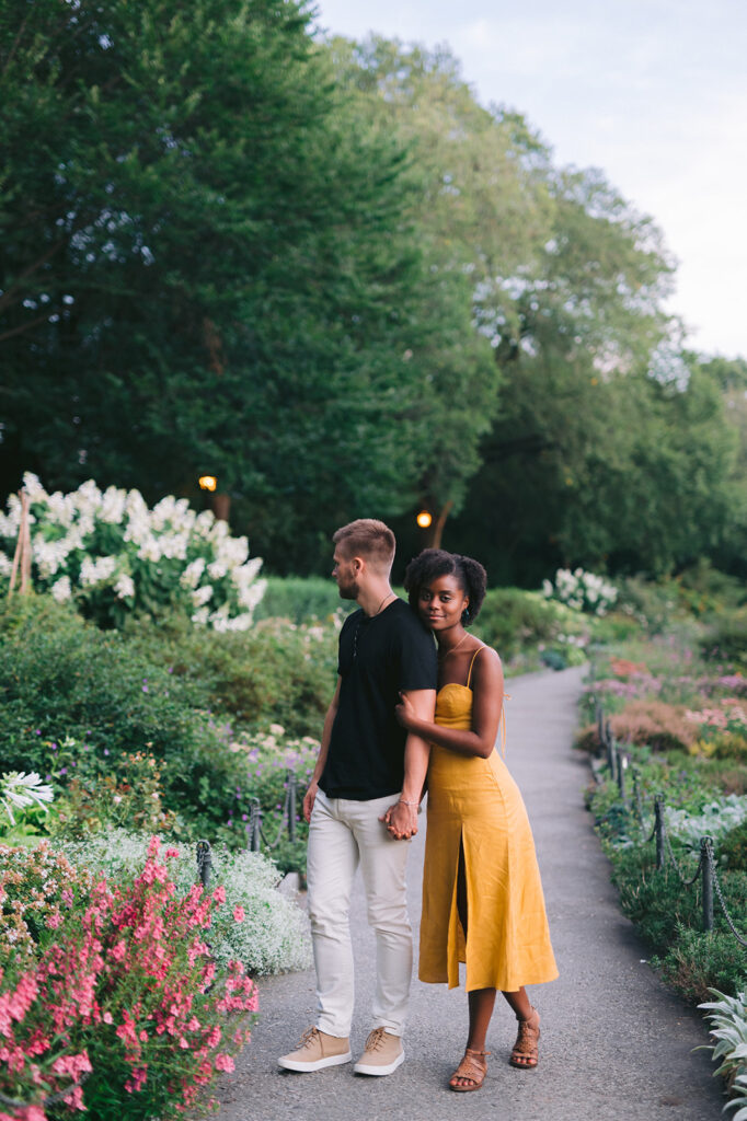 Couple walking down the paved walkway surrounded by lush gardens in New York Cities Washington Heights park. 