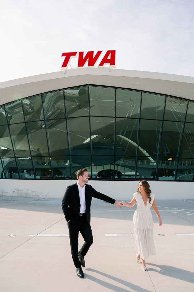 Couple walking on the tarmac at TWA Hotel for their engagement photoshoot.