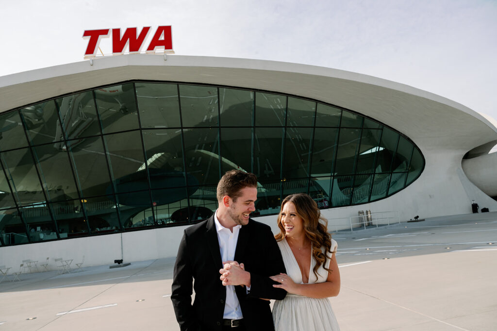 Candid couple walking on the tarmac at TWA Hotel for their retro engagement session.