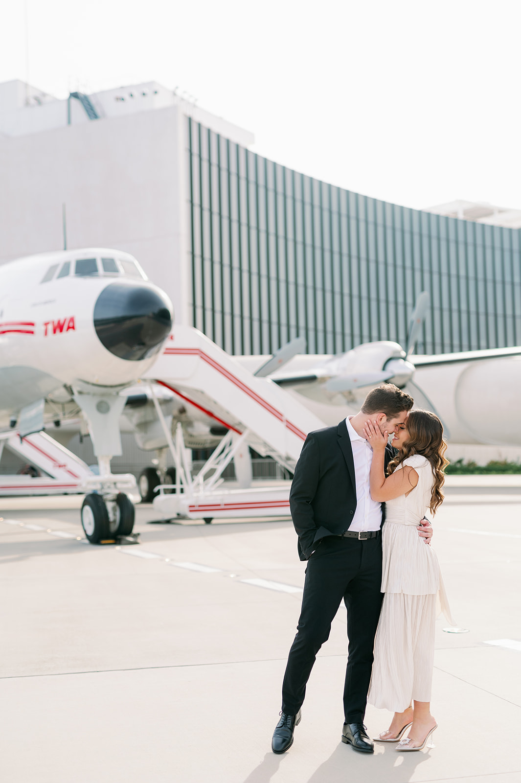 Stylish couple kissing on the tarmac of the TWA Hotel at JFK airport with the Connie Aircraft in the background.