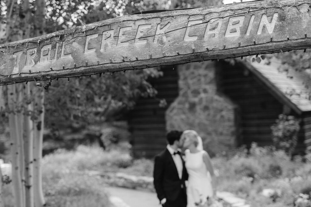 Bride and groom kissing under the Trail Creek Cabin sign during their wedding in Sun Valley, Idaho.