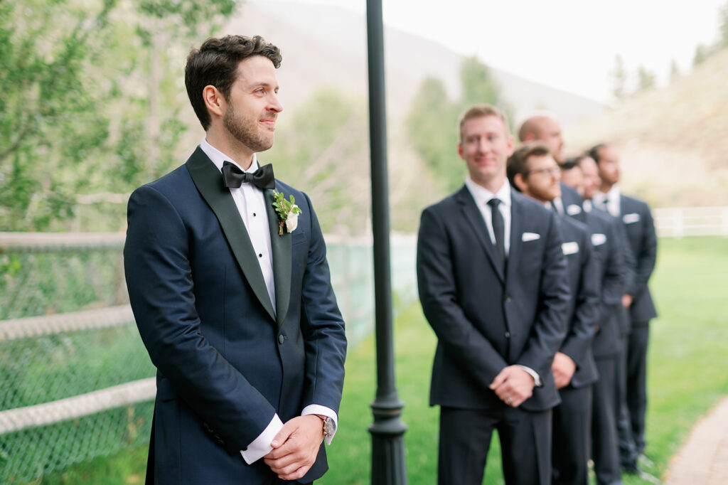 Groom watching his bride walk down the aisle with his groomsmen looking at him.