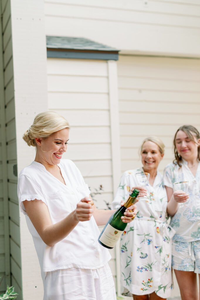 A bride and her bridesmaids popping a bottle of champagne.