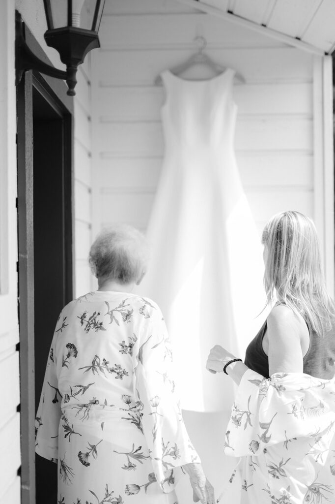 A bride's mom and grandma admiring her wedding dress hanging on a wooden hanger.