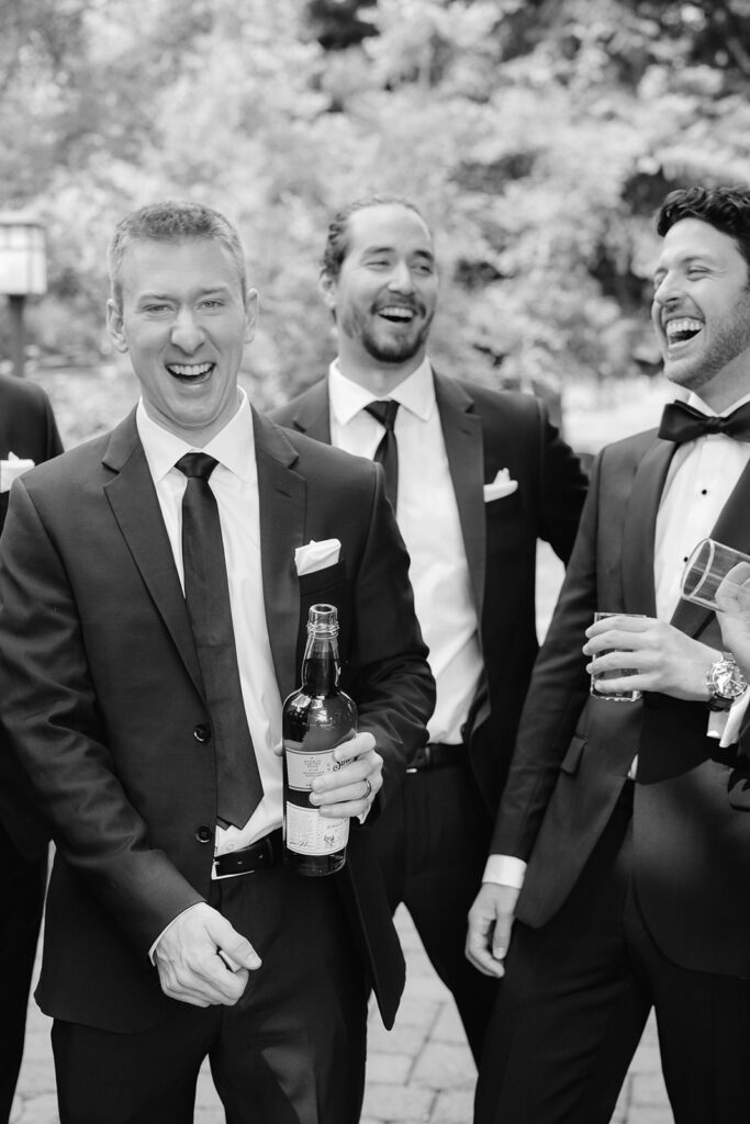 Groom and groomsmen laughing and having a drink.