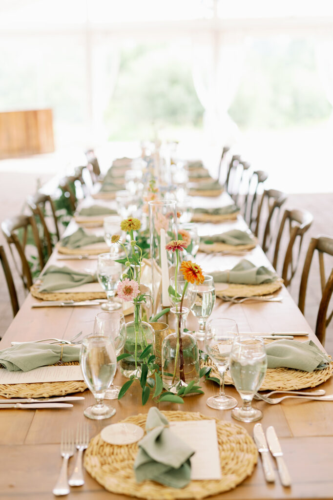 Rustic wedding reception tablescape with wicker chargers and sage green napkins.