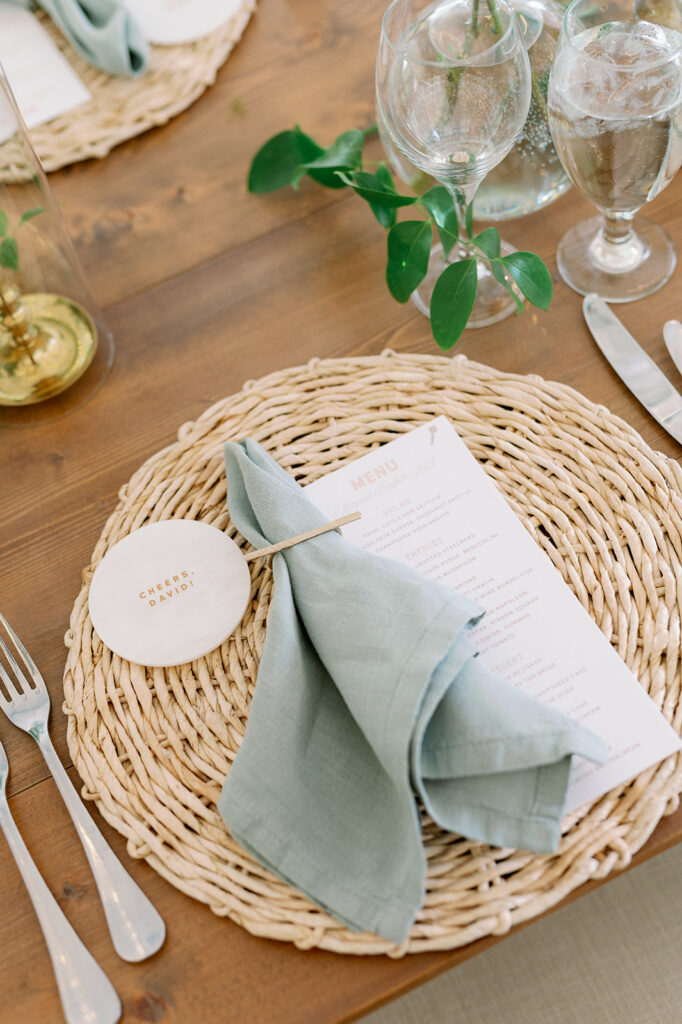 Wedding reception table setting with wicker chargers and sage green napkins.