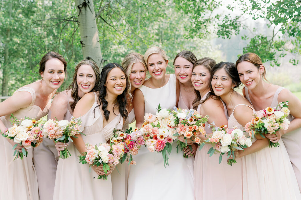 Bridal party portrait with neutral mismatched bridesmaid dresses and pastel floral bouquets.